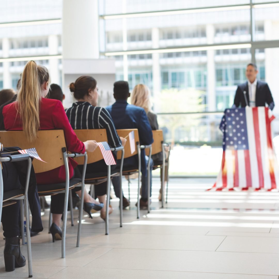 Front view of mixed race businessman speaks at a business seminar in office building with american flag